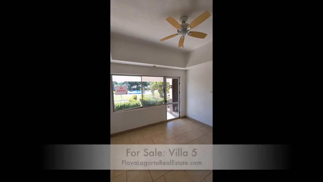 Bedroom with ceiling fan, large front window, and glass door opening toward the patio