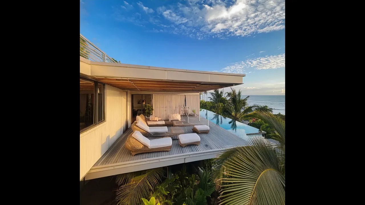 Covered terrace with cushioned outdoor seating overlooking ocean and pool edge