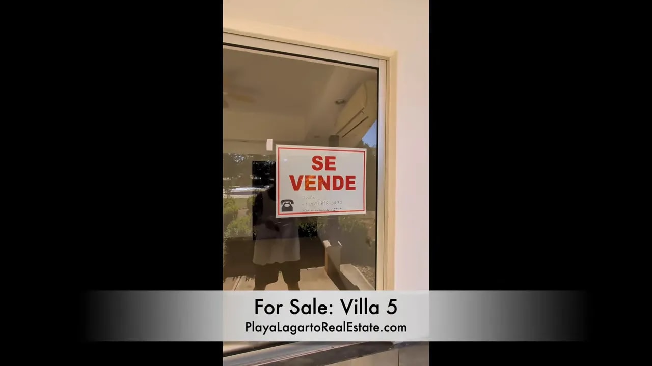 Large window with se vende sign posted on the glass and reflection of the patio area
