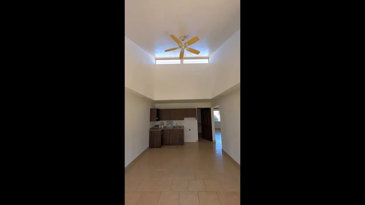 Open living area with high ceiling, ceiling fan, upper light openings, and kitchen at the back