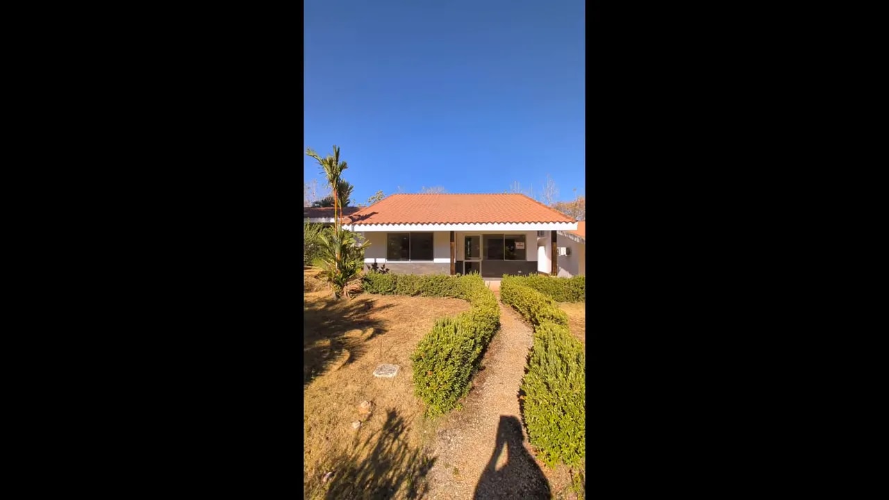 Straight-on view of the villa facade with walkway and trimmed hedges leading to the covered patio